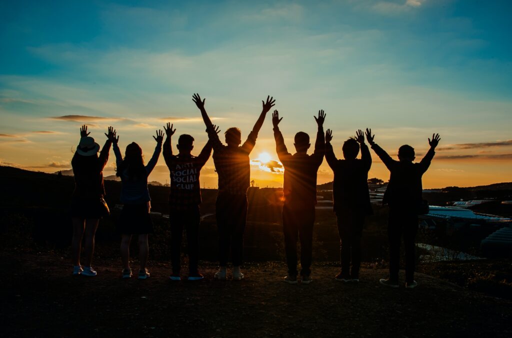 Group Of People Facing The Sunset While There Hands In Air